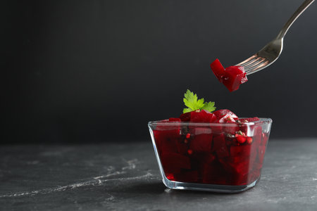 Pickled beets and fork over glass bowl on dark marble table, space for textの写真素材