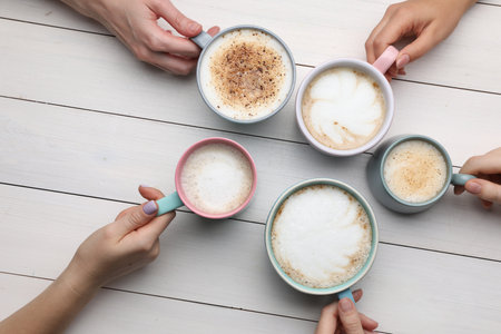 People holding different cups with aromatic hot coffee at white wooden table, top viewの写真素材