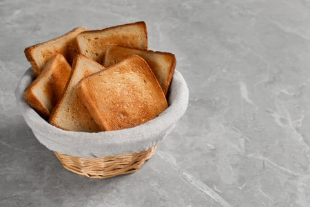 Wicker basket with slices of delicious toasted bread on gray marble tableの写真素材