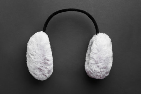 Stylish winter earmuffs on black background, top view