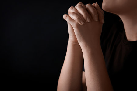 Woman holding hands clasped while praying against black background, closeup. Space for textの写真素材