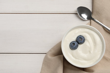 Bowl of yogurt with blueberries served on white wooden table, flat lay. Space for textの写真素材