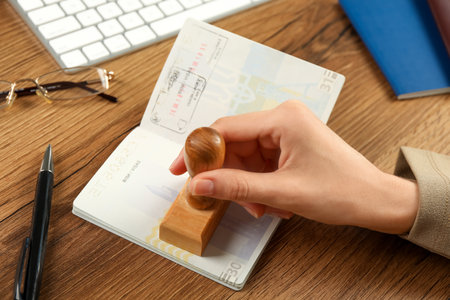 Moldova, Ceadir-Lunga - June 13, 2022: Woman stamping visa page in passport at wooden table, closeup