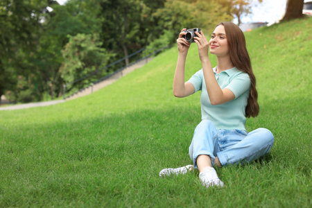 Young woman with camera taking photo on green grass outdoors, space for text. interesting hobbyの写真素材