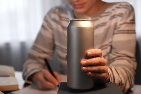 Tired young woman with energy drink studying at home, closeup