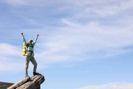 Young woman with backpack on rocky peak in mountains. Space for textの写真素材