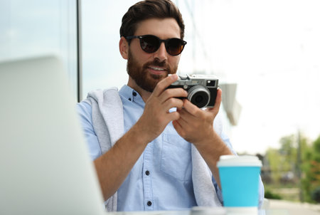 Man with camera, coffee and laptop in outdoor cafe. interesting hobby