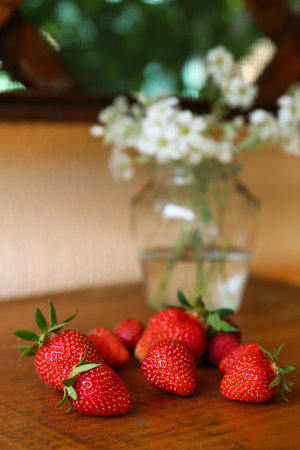 Fresh ripe strawberries and bouquet of beautiful flowers on wooden table, closeupの写真素材