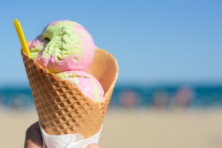 Little girl holding waffle cone with scoops of delicious colorful ice cream at beach on sunny summer...