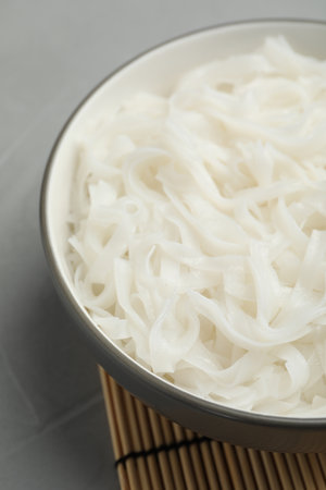 Bowl with cooked rice noodles on light gray table, closeup