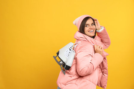 Happy woman with ice skates on yellow background. Space for text
