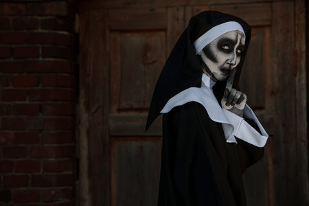 Portrait of scary devilish nun near red brick wall, space for text. halloween party lookの写真素材