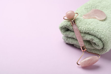 Natural face roller, towel and gua sha tool on pink background. Space for textの写真素材