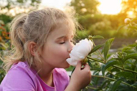 Cute little girl sniffing blooming peony outdoorsの写真素材