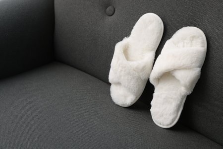Soft white slippers on gray sofa, space for text