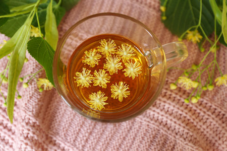 Glass cup of aromatic tea with linden blossoms on pink cloth, flat layの写真素材