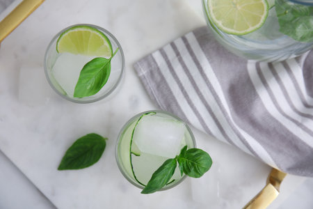 Tasty fresh cucumber water with sliced lime and basil on white marble table, flat layの写真素材