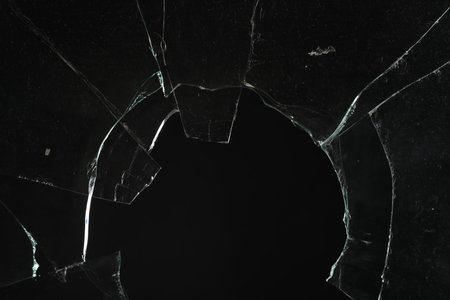 Close up view of broken glass with cracks on black background