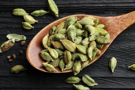 Spoon with dry cardamom pods on black wooden table, top viewの写真素材