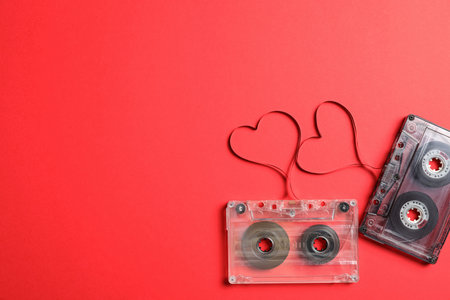 Music cassettes and hearts made of tape on red background, flat lay with space for text. Listening...
