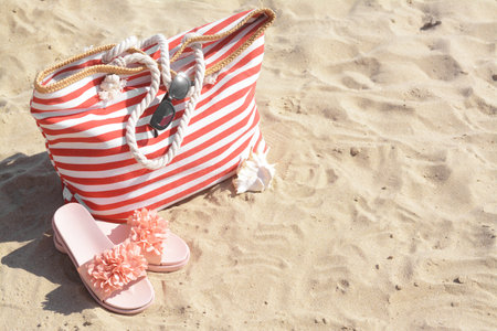 Stylish striped bag with slippers and sunglasses on sandy beach. Space for textの写真素材