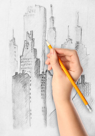 Woman drawing sketch of cityscape with graphite pencil on white paper, closeupの写真素材