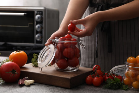 Woman tomatoes into glass jar at putting kitchen table, closeup. pickling vegetablesの写真素材