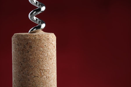 Corkscrew with wine cork on dark red background, closeup. Space for text