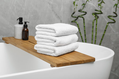 Stacked towels and personal care products on tub tray in bathroom