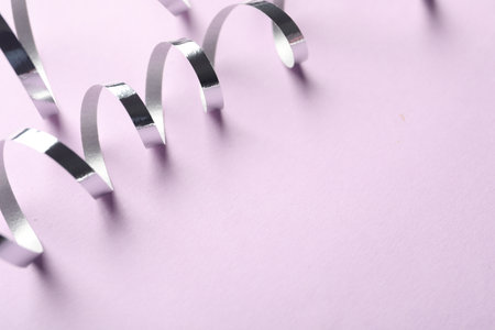 Shiny serpentine streamers on lilac background, closeup. Space for textの写真素材
