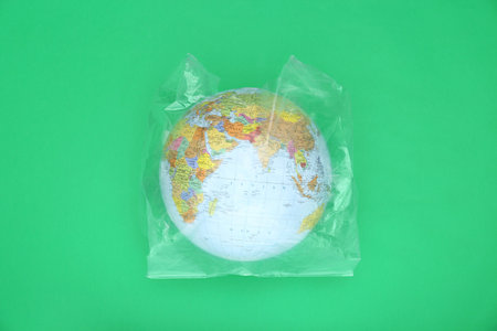 Globe in plastic bag on light green background, top view. environmental conservationの写真素材
