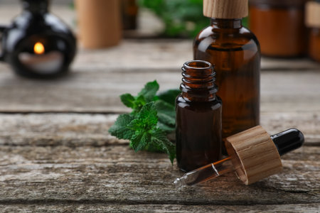 Bottles of mint essential oil and fresh leaves on wooden table, closeup. Space for textの写真素材