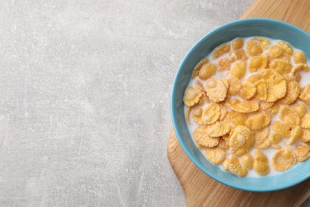 Bowl with tasty cornflakes and milk on light gray table, top view. Space for text