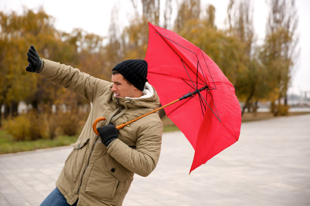 Man with red umbrella caught in the thick of wind outdoorsの写真素材