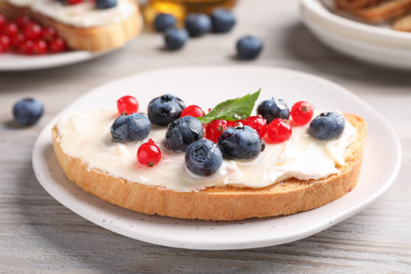 Tasty sandwiches with cream cheese and berries on white wooden table, closeup
