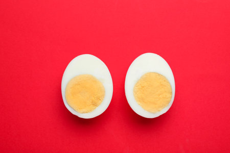 Halves of fresh hard boiled egg on red background, flat layの写真素材