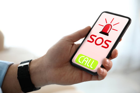 Man holding smartphone with emergency call SOS on screen indoors, closeupの写真素材