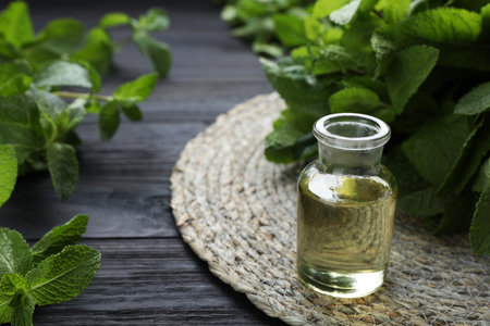 Bottle of mint essential oil and green leaves on black wooden table, closeup. Space for textの写真素材