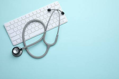 Computer keyboard with stethoscope on turquoise background, top view. Space for text
