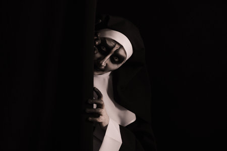 Scary devilish nun hiding on black background, space for text. halloween party lookの写真素材