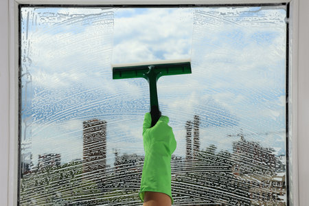 Woman cleaning glass with squeegee indoors, closeup