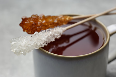 Sticks with sugar crystals and cup of tea on table, closeupの写真素材