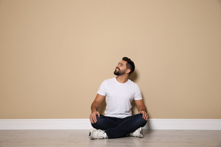Young man sitting on floor near beige wall indoorsの写真素材
