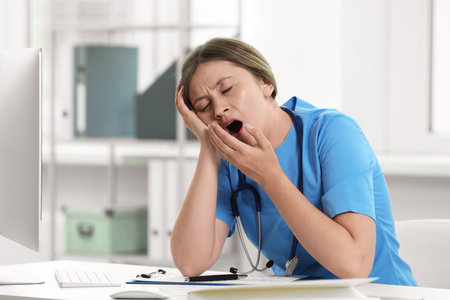 Exhausted doctor yawning at workplace in hospitalの写真素材