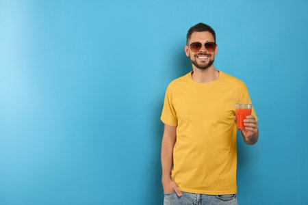 Man holding glass of delicious juice on light blue background, space for textの写真素材