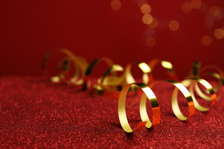 Shiny golden serpentine streamers on red table against blurred lights. Space for textの写真素材