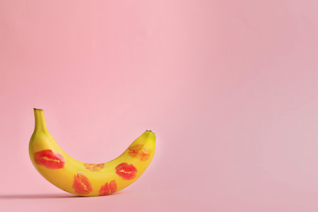 Banana covered with red lipstick marks on light pink background, space for text. Potency conceptの写真素材