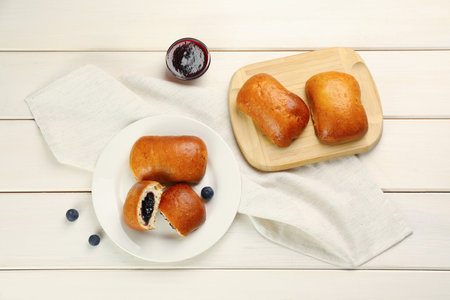 Delicious baked patties, jam and blueberries on white wooden table, flat lay