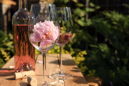 Bottle and glasses of rose wine near beautiful peonies on wooden table in gardenの写真素材