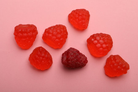 Delicious gummy candies and fresh raspberry on pink backgroundの写真素材